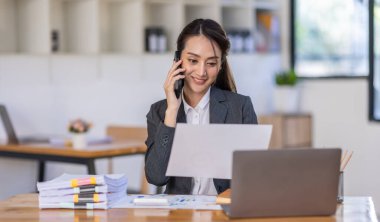 Asyalı kadın iş analisti mali danışman telefon eder ve istatistik raporu hazırlar. Çalışma masasında çalışırlar. Asyalı iş kadını ofiste belgelerle çalışır..