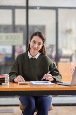 Neşeli Asyalı iş kadını çalışma alanı ofisinde çalışıyor. Ofisteki ahşap masada matematik finansmanı yapmak, vergi, muhasebe, finansal konsebe.