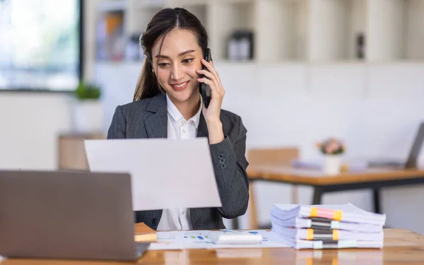 Asyalı kadın iş analisti mali danışman telefon eder ve istatistik raporu hazırlar. Çalışma masasında çalışırlar. Asyalı iş kadını ofiste belgelerle çalışır..