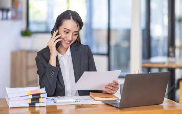 Asian female business analyst financial advisor call phone and preparing statistic report studying documents on work desk, Asian business woman work with documents in the office.