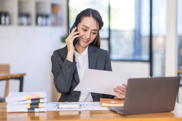 Asian female business analyst financial advisor call phone and preparing statistic report studying documents on work desk, Asian business woman work with documents in the office.