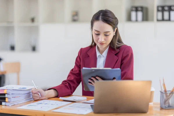 İş yerinde dizüstü bilgisayarda çalışan Asyalı bir kadın, kırmızı ceketli bir iş kadını dizüstü bilgisayarda çalışıyor finans, yatırım, ekonomi, tasarruf parası veya sigorta kavramı üzerinde çalışıyor.