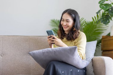 Gülümseyen genç Hintli serbest çalışan kadın cep telefonu kullanıyor sosyal medya ağlarını kontrol ediyor ya da evdeki yatakta oturan mesajları dinliyor. Çevrimiçi dijital iletişim, sıkı çalışma gününden sonra dinlenme