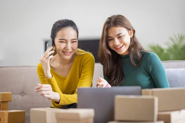 İki Asyalı kadın başlangıç için küçük işletme KOBİ girişimcisi dizüstü bilgisayarda paket kutusuyla evde çalışıyor, çevrimiçi pazarlama paketleme ve KOBİ fikri sunuyor