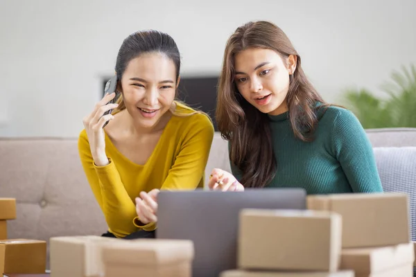 stock image Two Asian women to Startup small business SME entrepreneur of freelance working on laptop computer with parcel box on table laptop at home, online marketing packaging and delivery SME idea concept