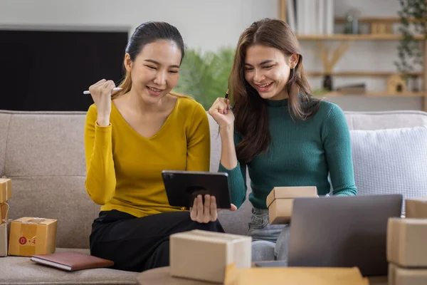 Stock image Two Asian women to Startup small business SME entrepreneur of freelance working on laptop computer with parcel box on table laptop at home, online marketing packaging and delivery SME idea concept