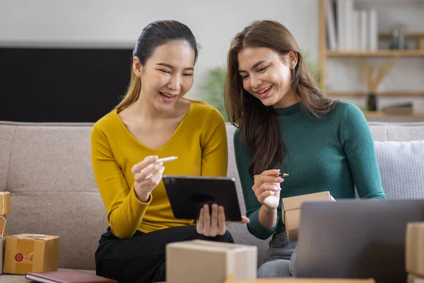 Stock image Two Asian women to Startup small business SME entrepreneur of freelance working on laptop computer with parcel box on table laptop at home, online marketing packaging and delivery SME idea concept