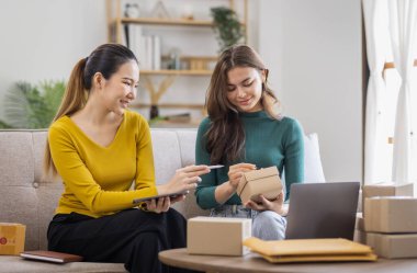 İki Asyalı kadın başlangıç için küçük işletme KOBİ girişimcisi dizüstü bilgisayarda paket kutusuyla evde çalışıyor, çevrimiçi pazarlama paketleme ve KOBİ fikri sunuyor