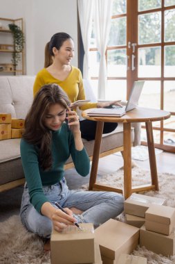 İki Asyalı kadın başlangıç için küçük işletme KOBİ girişimcisi dizüstü bilgisayarda paket kutusuyla evde çalışıyor, çevrimiçi pazarlama paketleme ve KOBİ fikri sunuyor