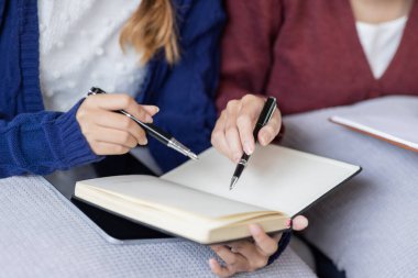 Genç, mutlu, gülümseyen, kulaklık takan iki Asyalı öğrenci üniversite kampüsünde ya da sanal ofiste bilgisayarla sohbet ediyorlar. Üniversiteli kız öğrenci uzaktan öğreniyor..