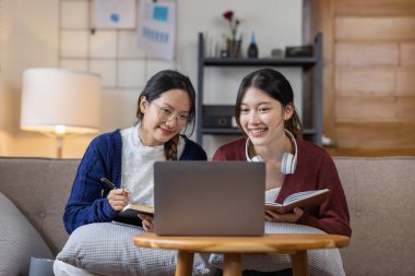 Genç, mutlu, gülümseyen, kulaklık takan iki Asyalı öğrenci üniversite kampüsünde ya da sanal ofiste bilgisayarla sohbet ediyorlar. Üniversiteli kız öğrenci uzaktan öğreniyor..