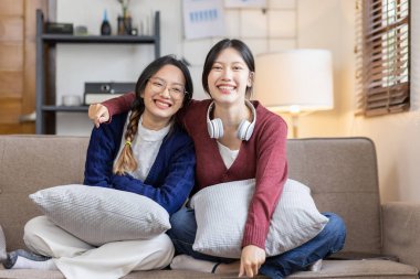 Genç, mutlu, gülümseyen, kulaklık takan iki Asyalı öğrenci üniversite kampüsünde ya da sanal ofiste bilgisayarla sohbet ediyorlar. Üniversiteli kız öğrenci uzaktan öğreniyor..