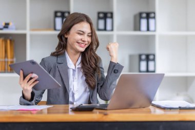 Mutlu Asyalı başarılı iş kadını iş yerinde akıllı telefon ve dizüstü bilgisayarla zafer kazanıyor..