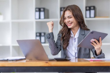 Mutlu Asyalı başarılı iş kadını iş yerinde akıllı telefon ve dizüstü bilgisayarla zafer kazanıyor..