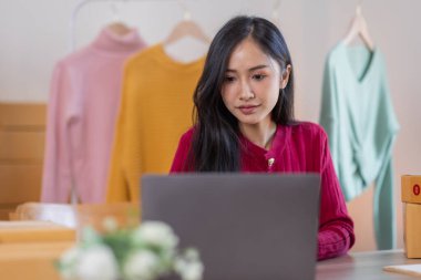 İnternette kıyafet satan Asyalı kadın KOBİ 'ler, evde telefon ve dizüstü bilgisayarla müşterilerin sorularını cevaplıyor, küçük işletme girişimciliği, Çevrimiçi ticaret, KOBİ konsepti.