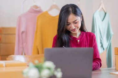 İnternette kıyafet satan Asyalı kadın KOBİ 'ler, evde telefon ve dizüstü bilgisayarla müşterilerin sorularını cevaplıyor, küçük işletme girişimciliği, Çevrimiçi ticaret, KOBİ konsepti.