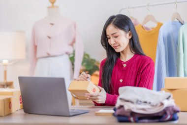 İnternette kıyafet satan Asyalı kadın KOBİ 'ler, evde telefon ve dizüstü bilgisayarla müşterilerin sorularını cevaplıyor, küçük işletme girişimciliği, Çevrimiçi ticaret, KOBİ konsepti.