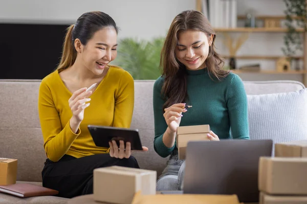 stock image Two Asian women to Startup small business SME entrepreneur of freelance working on laptop computer with parcel box on table laptop at home, online marketing packaging and delivery SME idea concept