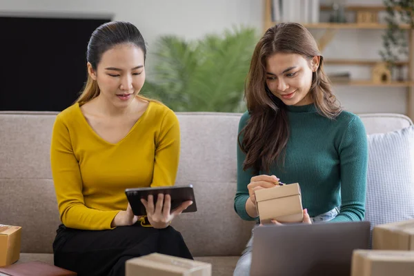 stock image Two Asian women to Startup small business SME entrepreneur of freelance working on laptop computer with parcel box on table laptop at home, online marketing packaging and delivery SME idea concept