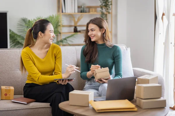 stock image Two Asian women to Startup small business SME entrepreneur of freelance working on laptop computer with parcel box on table laptop at home, online marketing packaging and delivery SME idea concept