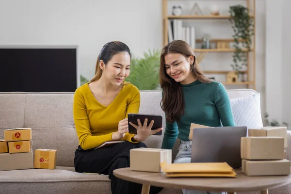 stock image Two Asian women to Startup small business SME entrepreneur of freelance working on laptop computer with parcel box on table laptop at home, online marketing packaging and delivery SME idea concept