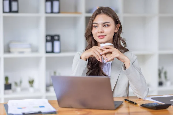 stock image Beautiful young smiling asian multiethnic woman working on laptop and drinking coffee in at workplace, Asia woman working document finance and calculator in her home office. Enjoying time at home.