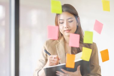 share idea, project successful, Business Asian business woman in meeting brainstorming and use post paper and writing note and stick on glass wall at workplace office.