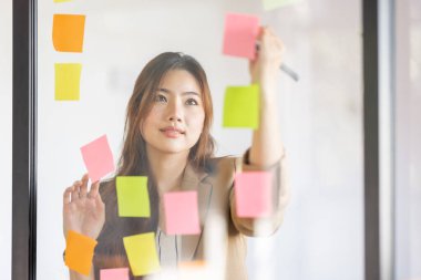 share idea, project successful, Business Asian business woman in meeting brainstorming and use post paper and writing note and stick on glass wall at workplace office.