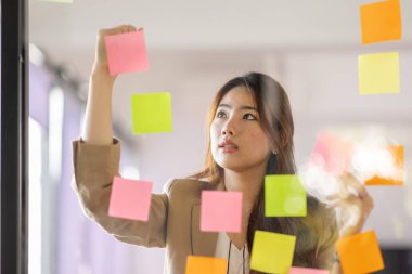 share idea, project successful, Business Asian business woman in meeting brainstorming and use post paper and writing note and stick on glass wall at workplace office.