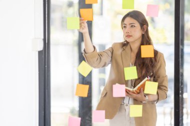 share idea, project successful, Business Asian business woman in meeting brainstorming and use post paper and writing note and stick on glass wall at workplace office.