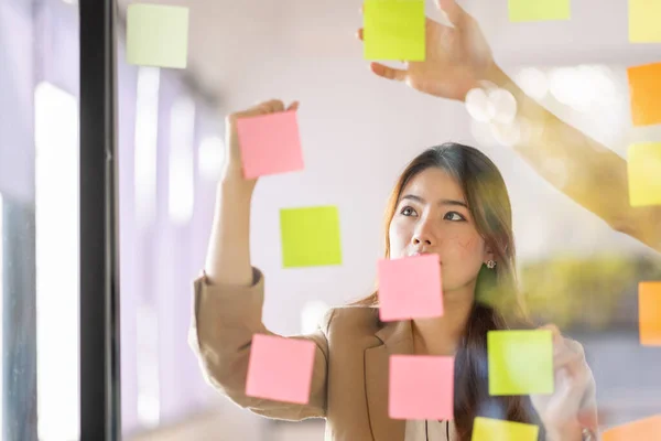 share idea, project successful, Business Asian business woman in meeting brainstorming and use post paper and writing note and stick on glass wall at workplace office.