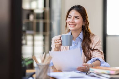 Image of young beautiful brooding Asian woman working with laptop while sitting at laptop in office, thinking of professional plan, project management, considering new business ideas.