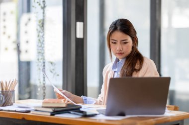 Thai Asian businesswoman working inside office with documents and laptop, worker paperwork calculates financial indicators smiling and happy with success and results of achievement and work