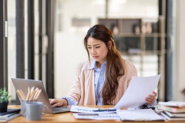 Thai Asian businesswoman working inside office with documents and laptop, worker paperwork calculates financial indicators smiling and happy with success and results of achievement and work