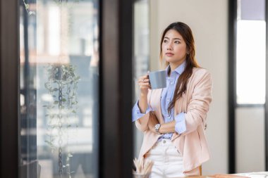Portrait of a charming young woman businessman in the office standing holding a Coffee cup in hand and looking away from camera