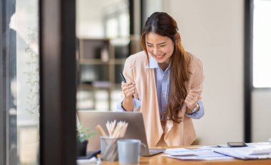 happy excited.Portrait of success business asian woman enjoy success with laptop on work desk. Authentic shot joyful asian girl got jackpot, Surprised and celebrating her victory.
