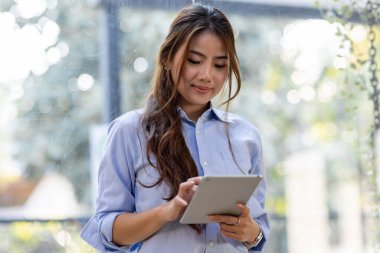 Young business Asian woman using tablet and standing near the window in workplace