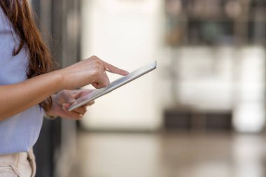 Young business Asian woman using tablet and standing near the window in workplace
