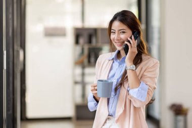 Young Office Asian Woman Talking to Someone on her Mobile Phone While Looking Into the Distance with Happy Facial Expression.