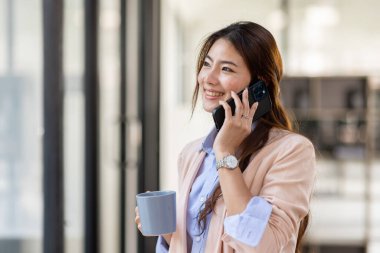 Young Office Asian Woman Talking to Someone on her Mobile Phone While Looking Into the Distance with Happy Facial Expression.
