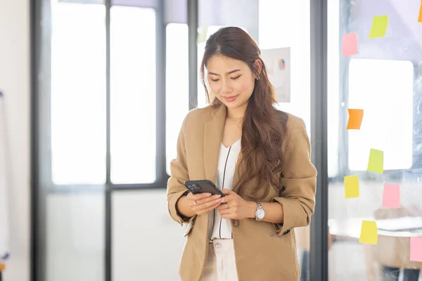 Smiling business asian woman using phone in office. Small business entrepreneur looking at her mobile phone and smiling.