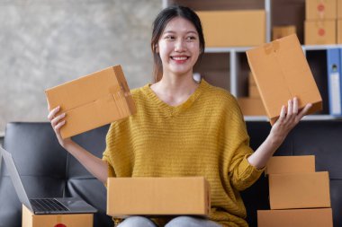 Startup SME small business entrepreneur of freelance Asian woman using a laptop with box Cheerful success Asian woman her hand lifts up online marketing packaging box and delivery SME idea concept