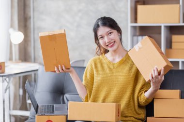 Startup SME small business entrepreneur of freelance Asian woman using a laptop with box Cheerful success Asian woman her hand lifts up online marketing packaging box and delivery SME idea concept