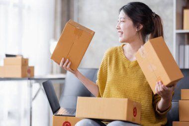 Startup SME small business entrepreneur of freelance Asian woman using a laptop with box Cheerful success Asian woman her hand lifts up online marketing packaging box and delivery SME idea concept
