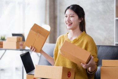 Startup SME small business entrepreneur of freelance Asian woman using a laptop with box Cheerful success Asian woman her hand lifts up online marketing packaging box and delivery SME idea concept