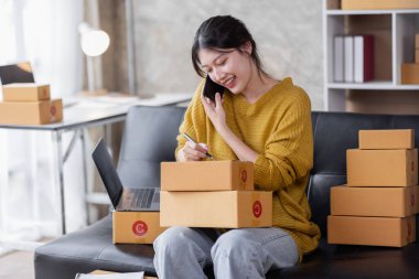 Startup SME small business entrepreneur of freelance Asian woman using a laptop with box Cheerful success Asian woman her hand lifts up online marketing packaging box and delivery SME idea concept