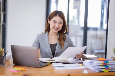 Young asian business woman manager accounting analyst checking bills, analyzing sales statistics management, taxes financial data documents or marketing report papers working in office using laptop.