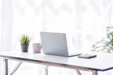 Laptop Computer, notebook, and eyeglasses sitting on a desk in a large open plan office space after working hours