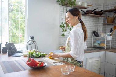 Portrait of attractive asian japanese woman in kitchen at home, young girl browsing website on tutor cooking class and doing for kitchen, cutting vegetables, cooking, cooking concept.