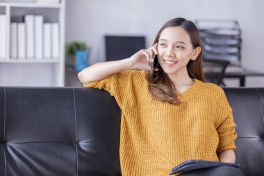 Beautiful Young Asian woman using smartphone on sofa at home, shopping online with internet in happy mood and Relax part time concept